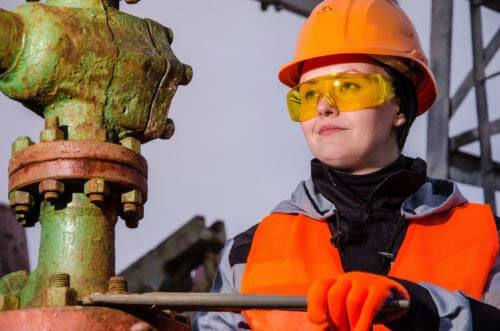 Woman engineer in the oil field repairing wellhead with the wrench wearing orange helmet and work clothes. Oil and gas concept.