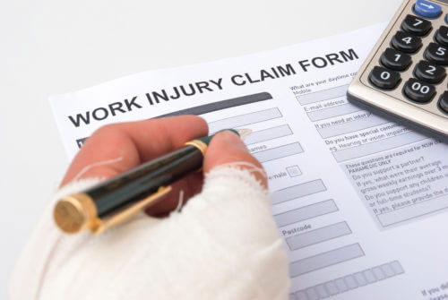 Closeup of a bandaged hand filling out a work injury claim form