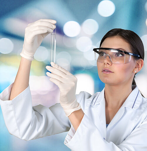 Student in lab coat and gloves looking at a test tube