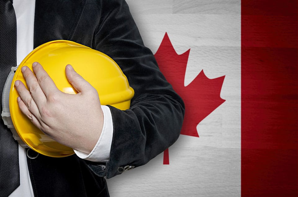 Canadian employee holding hard hat in front of Canadian flag